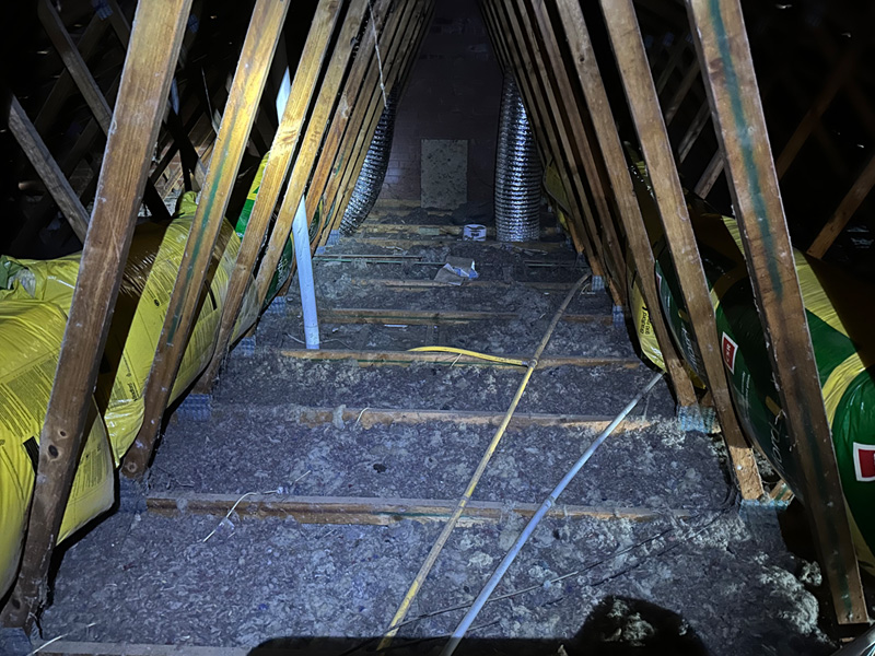 Before: roof space with old, thin loose-fill insulation between timber trusses
