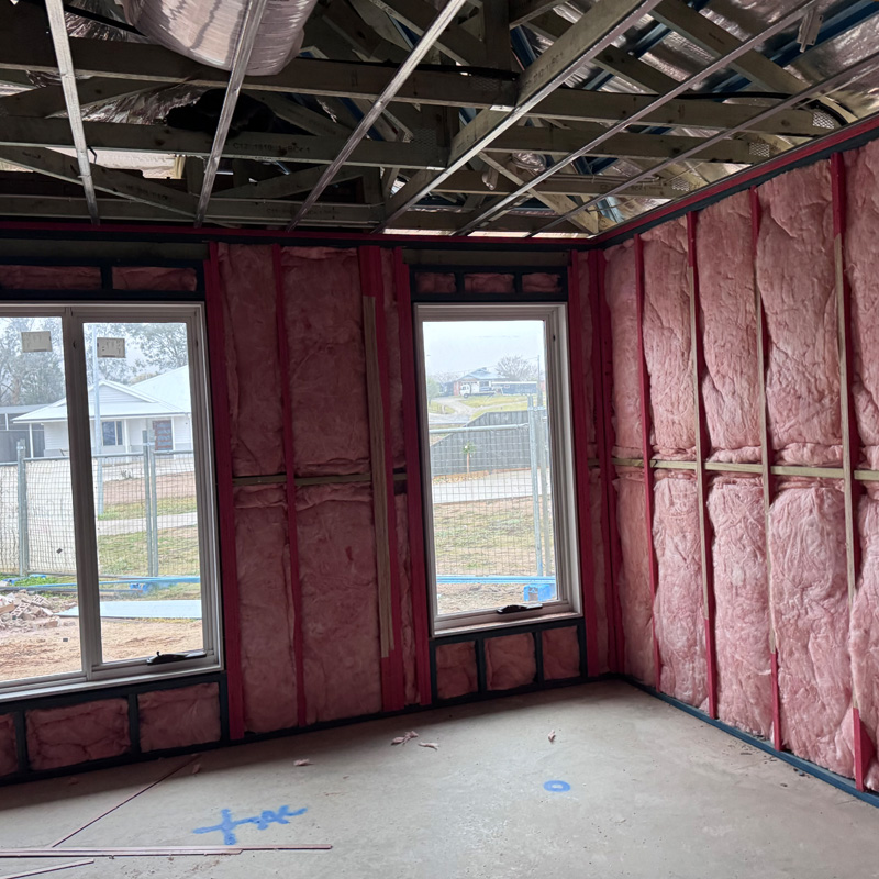 Pink insulation batts in the wall frames around two windows of a new home