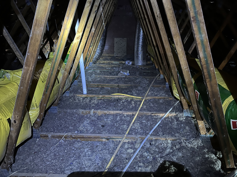 Roof space with old, thin loose-fill insulation between timber trusses