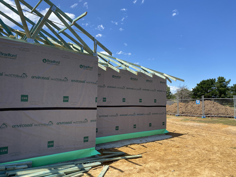 Two wall-wrapped house frames with roof trusses going up on a building site