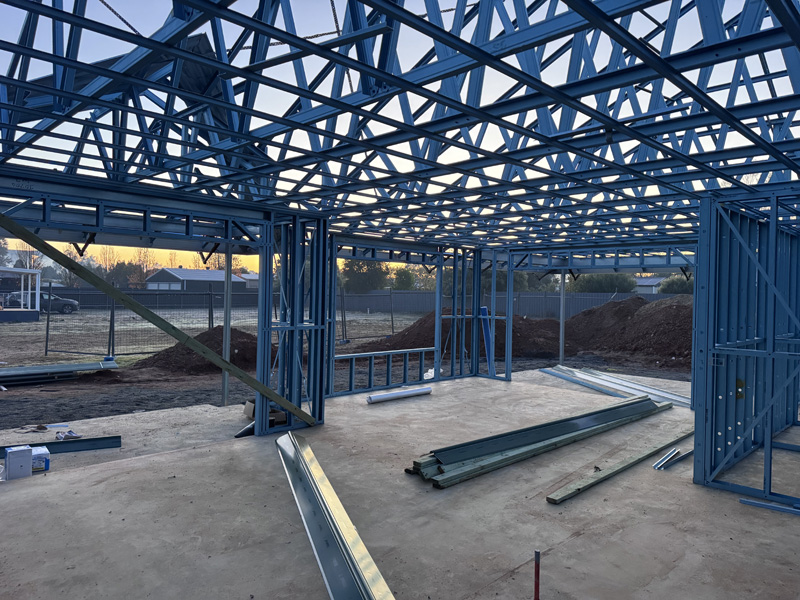Blue steel house frame and roof trusses on a concrete slab, before insulation