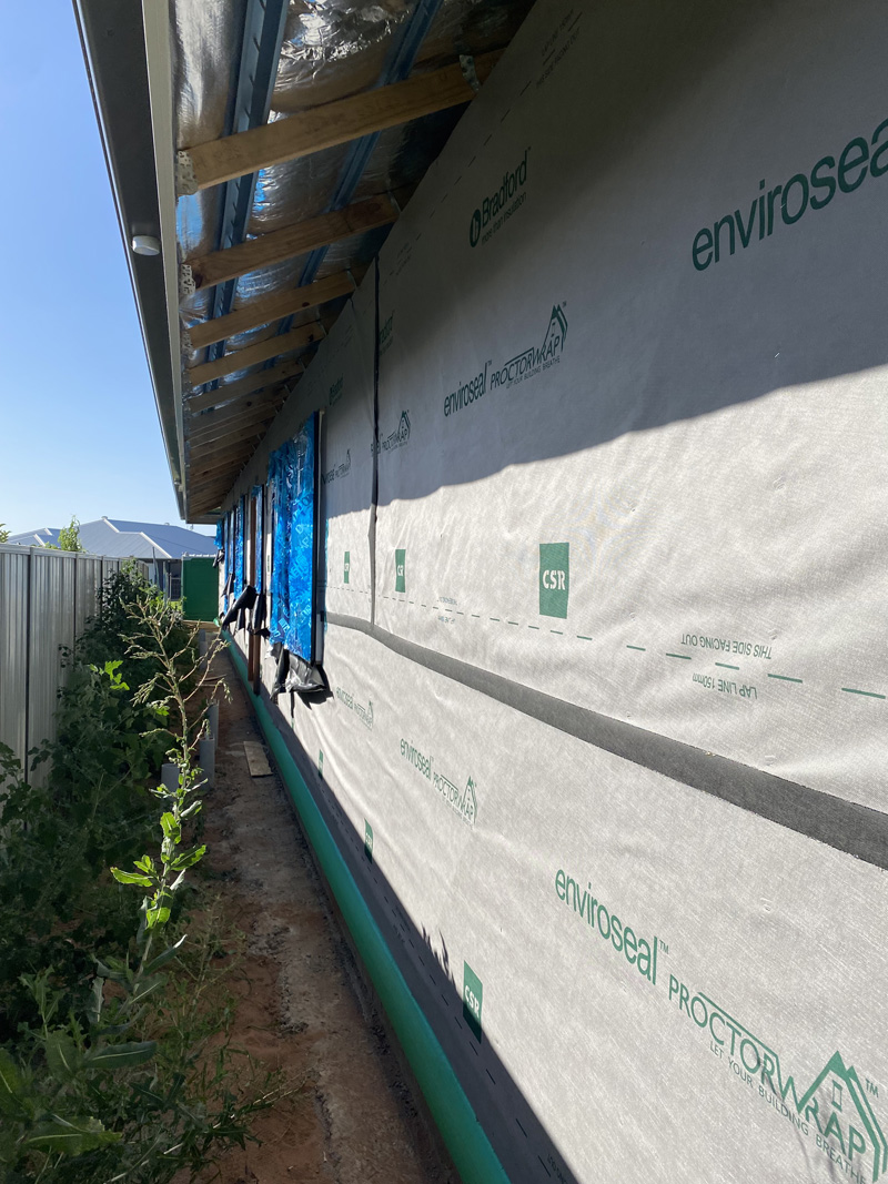 Wall wrap along the side of a new home beside a narrow garden bed, upright view