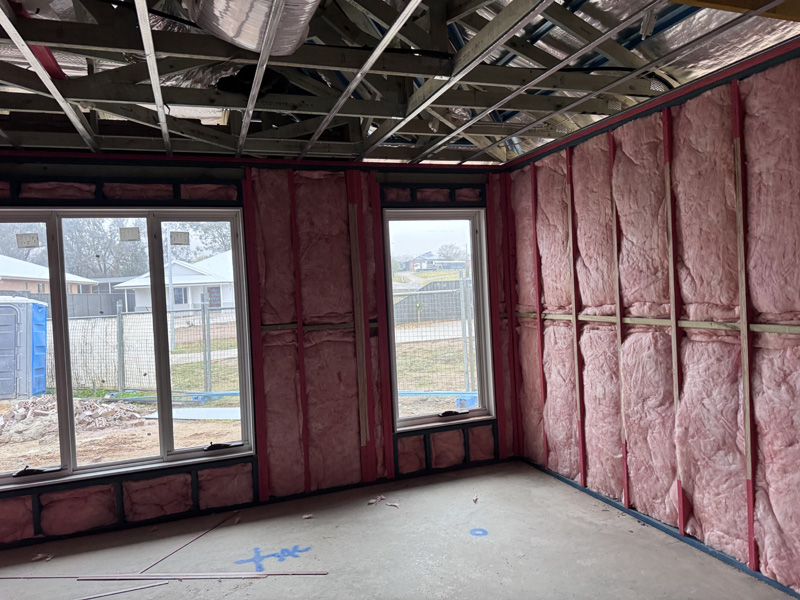 Pink insulation batts in the wall frames around two windows of a new home