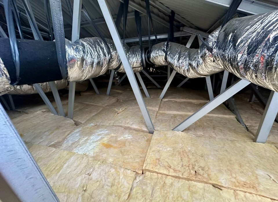 Ceiling insulation batts under silver ducting in a steel-framed roof space