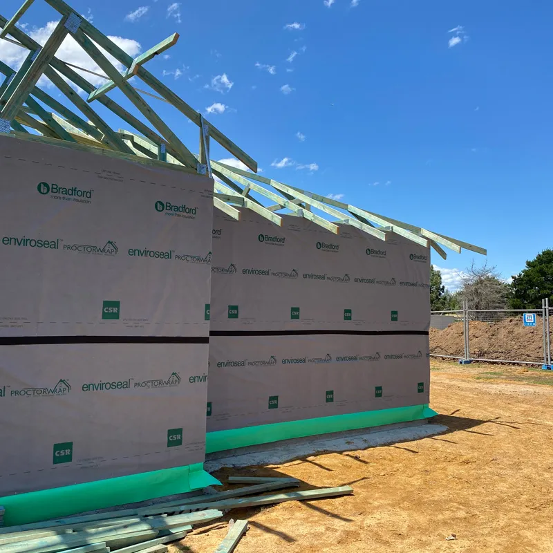 Two wall-wrapped house frames with roof trusses going up on a building site