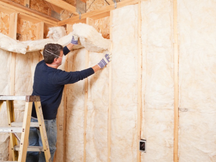 residential house wall insulation Man on a ladder fitting insulation batts into a timber-framed wall