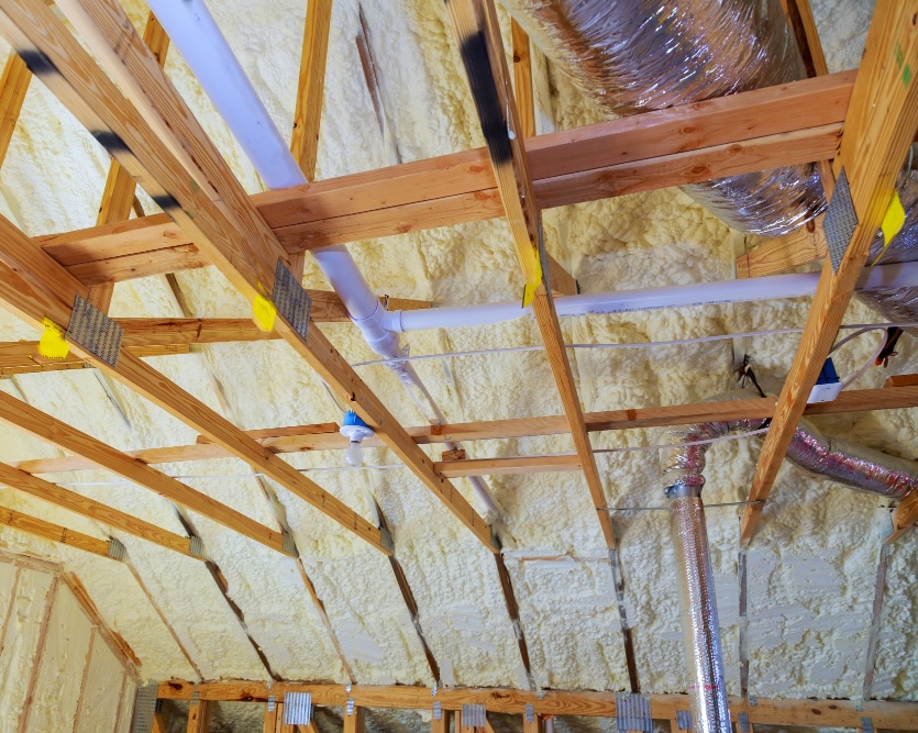 Close view of spray foam roof insulation around timber trusses, pipes and ducts