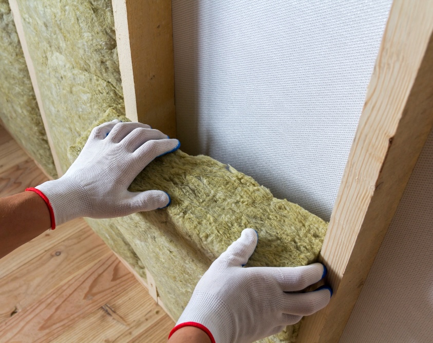 Gloved hands fitting a mineral wool batt between timber wall studs