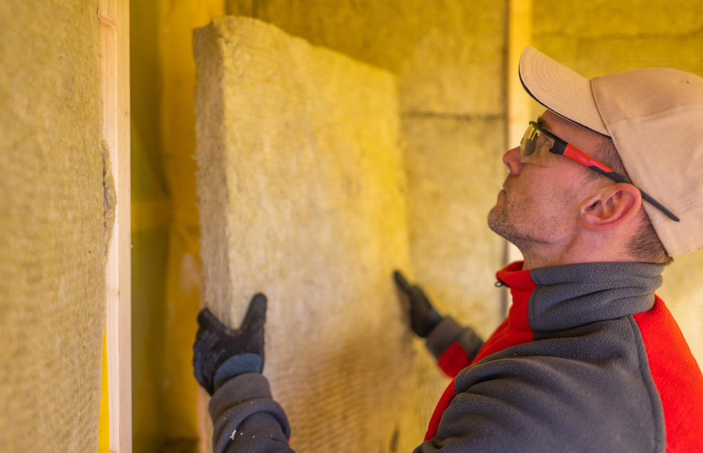 Insulation for New Builds Bright Installer in a cap and safety glasses fitting a mineral wool batt into a wall